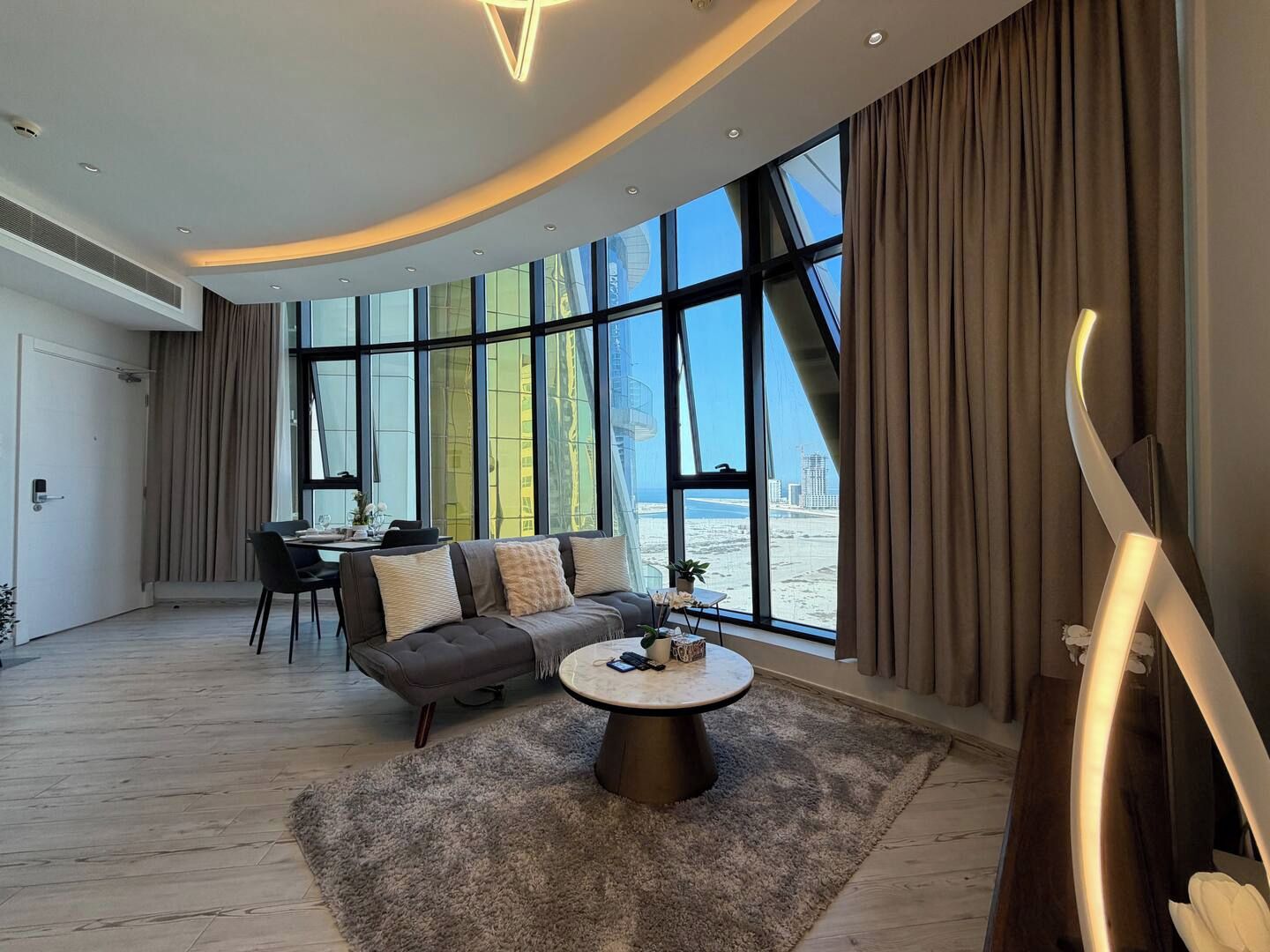 A modern living room with a curved ceiling, large windows, a sofa, a coffee table, and a dining area.