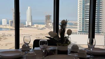 A dining table set with plates, glasses, and cutlery, overlooking a cityscape with high-rise buildings and a beach.