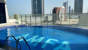 A rooftop swimming pool with a glass railing, surrounded by high-rise buildings.