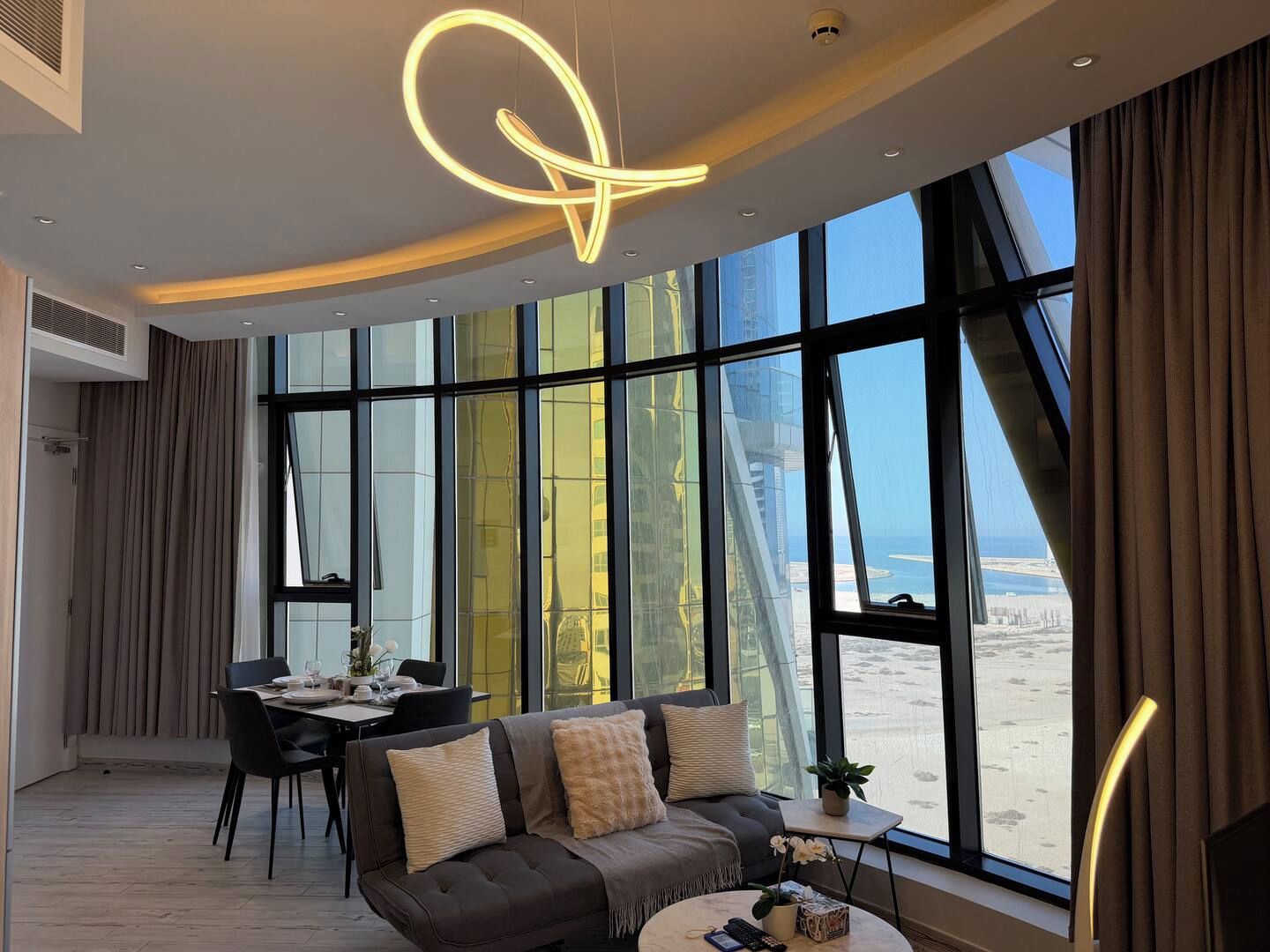 A modern interior with a dining area, a sofa, and large windows offering a view of the beach.