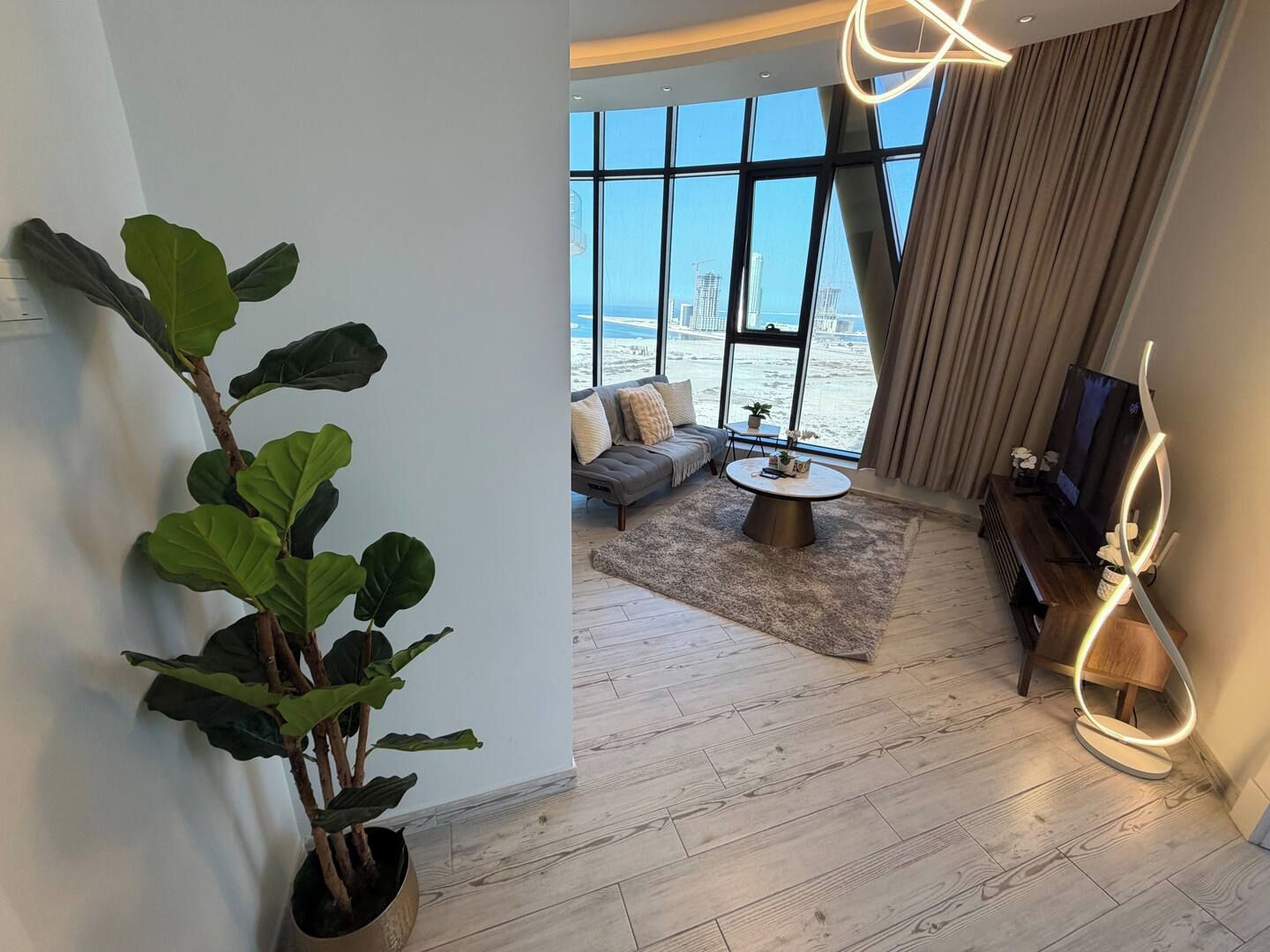 A modern living room with a large window, a sofa, a coffee table, and a TV.