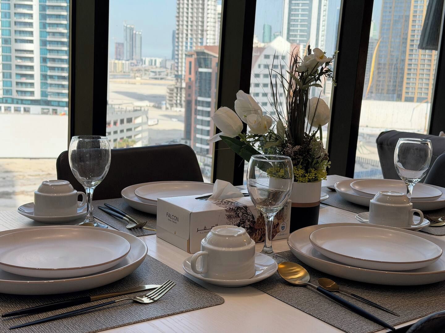 A table set for dining with white plates, glasses, and a vase of flowers.