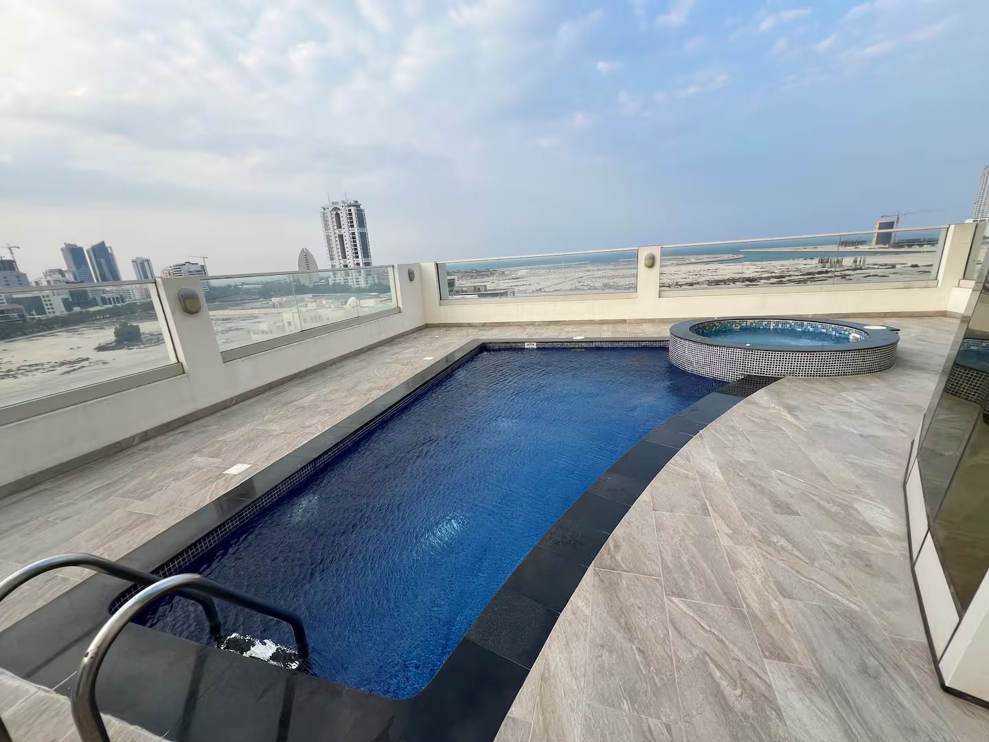 A rooftop swimming pool with a hot tub, surrounded by a cityscape view.