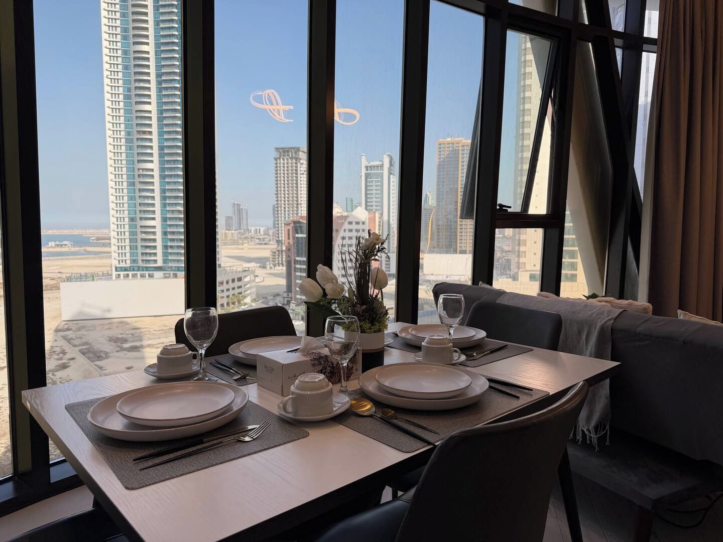 A dining table set for two with a view of a cityscape through large windows.