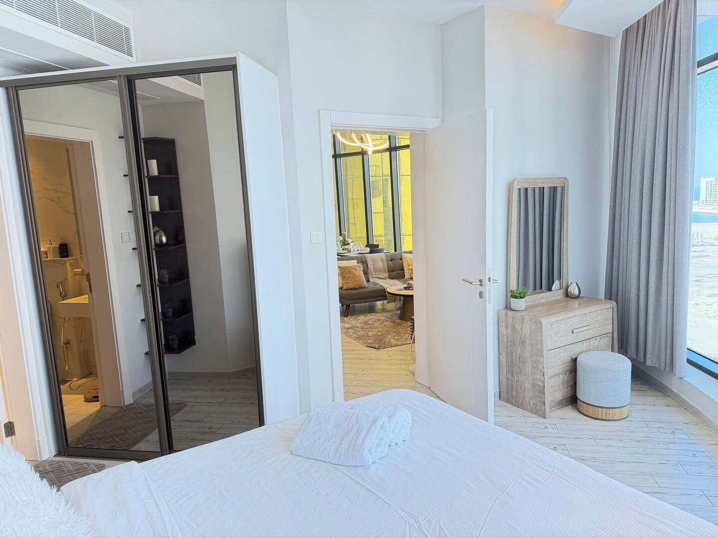 A modern hotel room with a bed, a vanity, a large window with curtains, and a view of the outdoors.