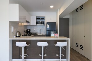 A modern kitchen with a central island, bar stools, a microwave, a refrigerator, and a coffee maker. - w* | Charming 1BR w/ Balcony in Miraflores (Miraflores)