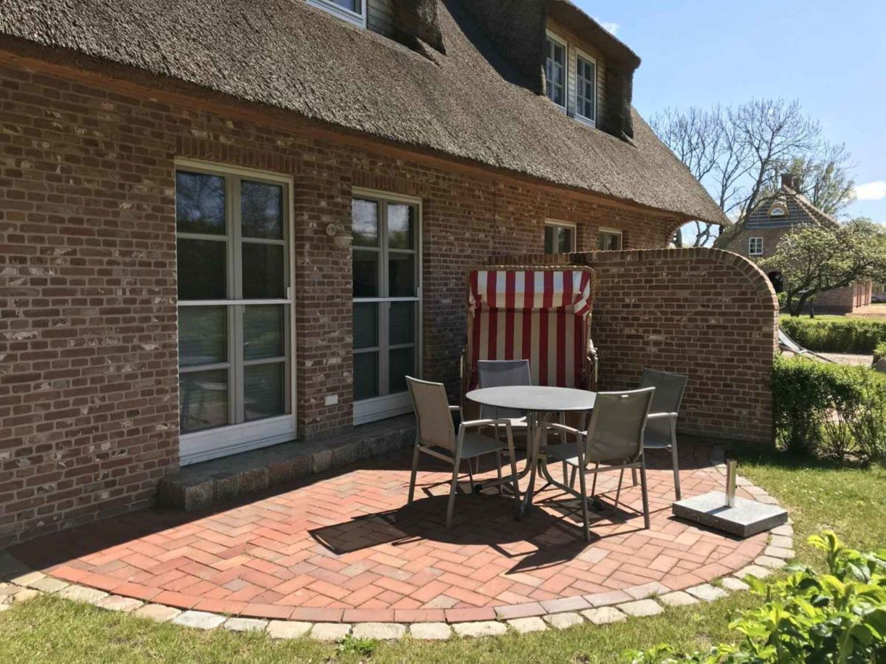Una casa in mattoni con tetto di paglia, un patio con tavolo e sedie e un tendaggio a righe.