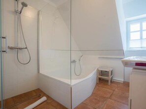 Ein modernes Badezimmer mit einer gläsernen Dusche, einer weißen Badewanne und einem kleinen Holzschemel.