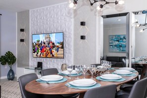 A modern dining area with a large flat-screen TV mounted on the wall, a round wooden table set for dining, and a large potted plant. - 3BR Townhome in Fiesta Key Near Disney Parks (Kissimmee)