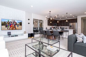 Uma sala de estar moderna com televisão de tela plana, uma mesa de centro de vidro e um sofá cinza.