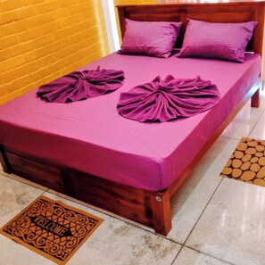 Ein Bett mit einer violetten Tagesdecke und Kissen, eine Fußmatte und ein hölzernes Kopfende.