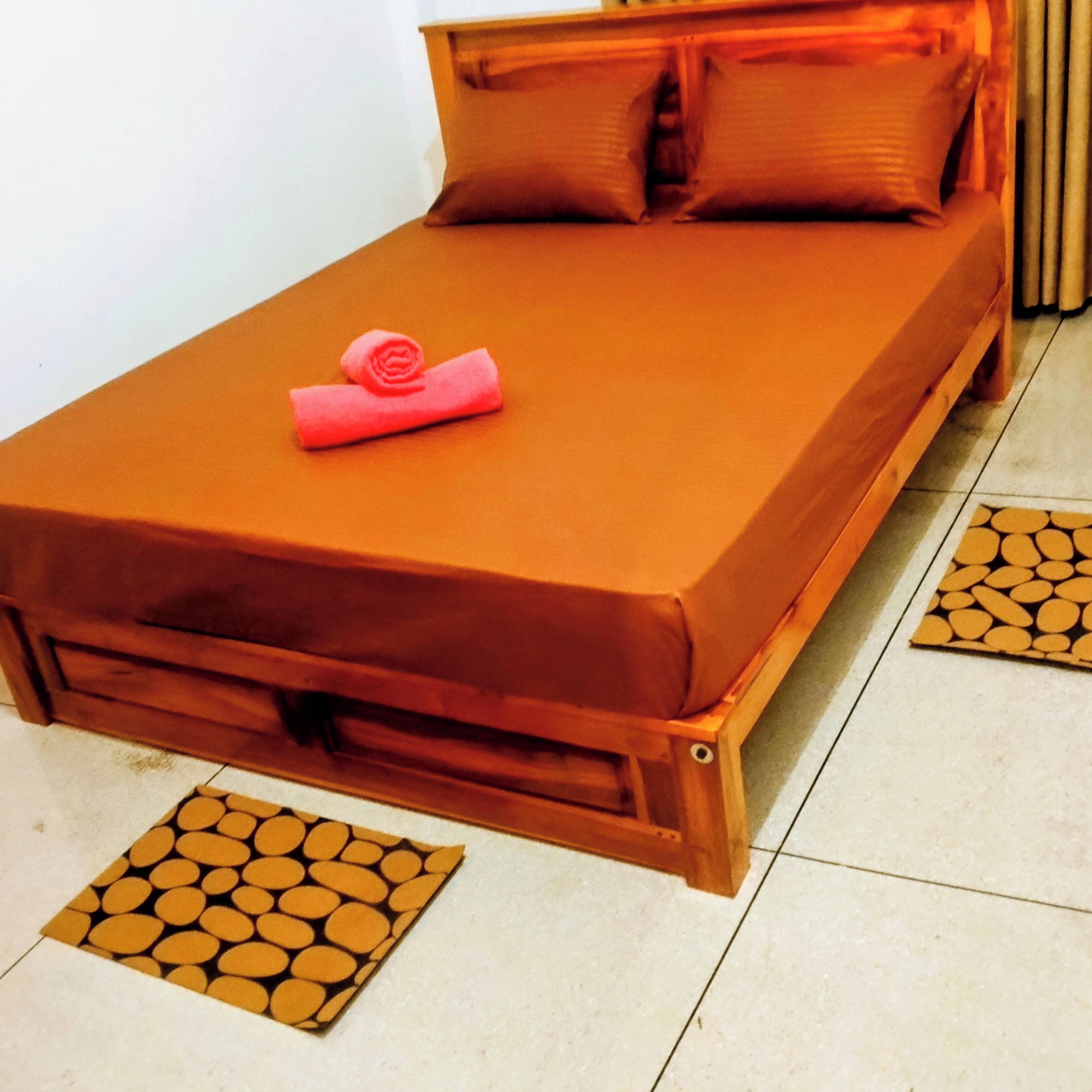 A single bed with a brown mattress and pillows, a pink towel, and a wooden headboard.