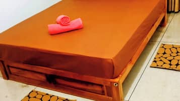 A single bed with a brown mattress and pillows, a pink towel, and a wooden headboard.