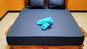 A bed with a dark blue mattress and pillows, a wooden headboard, and a patterned rug on the floor. - Guest House - Habarana (Habarana)
