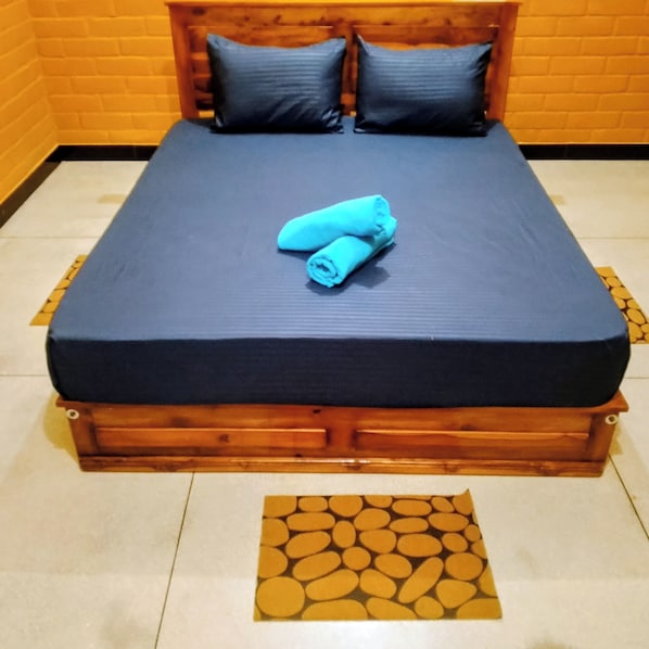 A bed with a dark blue mattress and pillows, a wooden headboard, and a patterned rug on the floor.