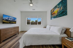 Una camera da letto con un letto, una cassettiera in legno, una ventola a soffitto, una finestra con vista e un quadro appeso al muro.