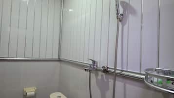Un baño con inodoro, dispensador de toallas de papel, ducha con cabezal de ducha manual y un recipiente de vidrio en la pared.