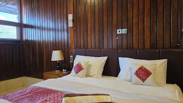 Une chambre d’hôtel avec un mur lambrissé en bois, un lit avec une literie blanche et des oreillers rouges, une table de chevet avec une lampe et une couvre-lit rouge à motifs.