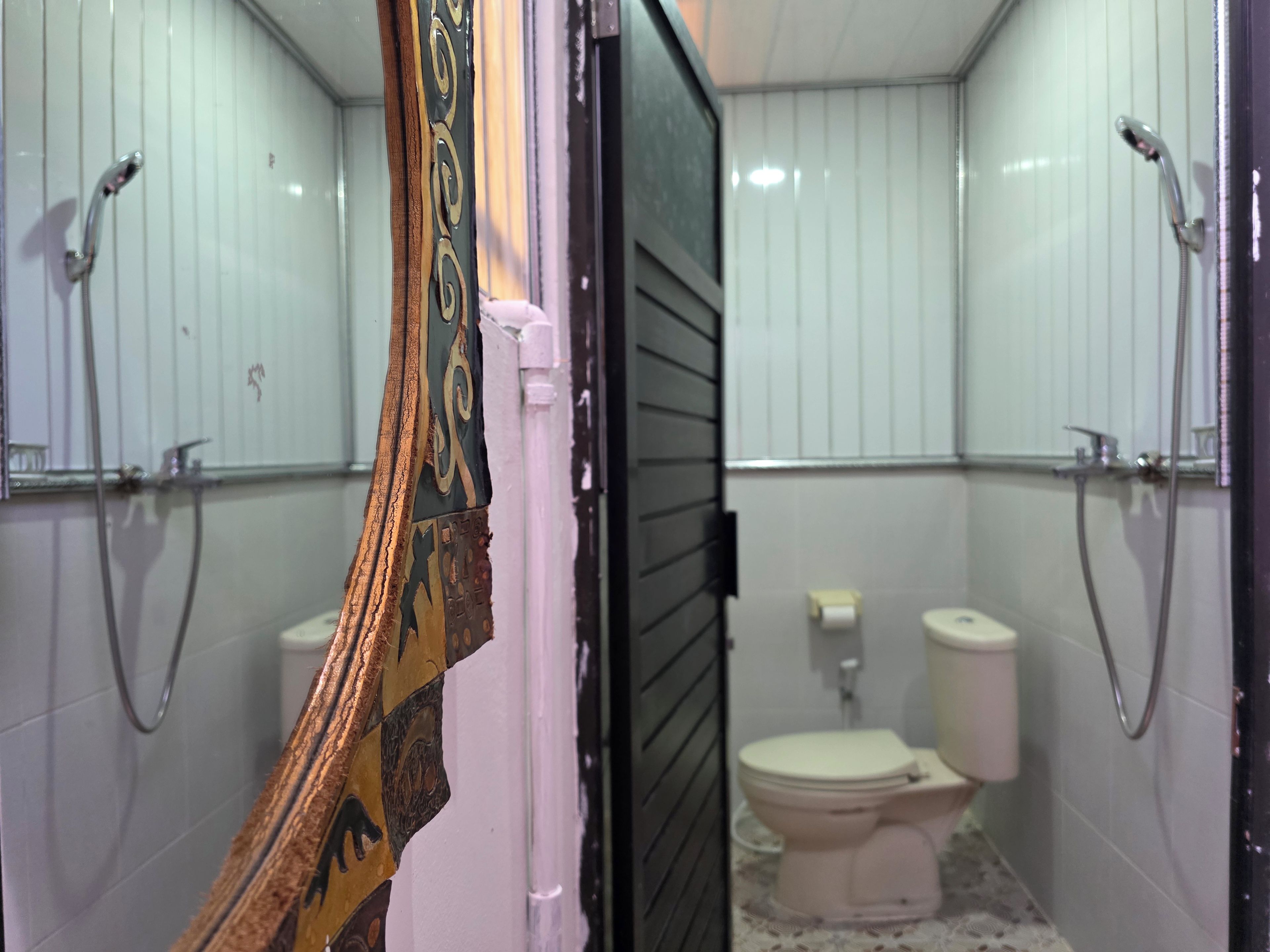 Un baño con paredes de azulejos blancos, un inodoro y dos cabezales de ducha.