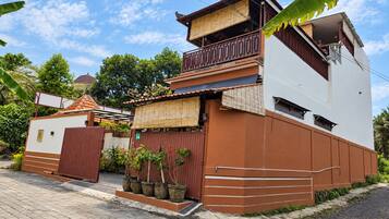 A two-story building with a balcony, a gated entrance, and potted plants.