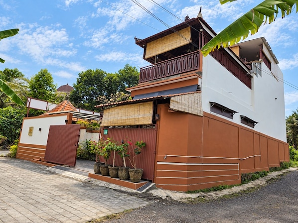 A two-story building with a balcony, a gated entrance, and potted plants.