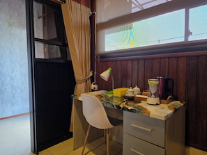 A small, cluttered workspace with a desk, chair, and various items including a lamp, a kettle, and containers. - Dahlia Moon Saba Beach (Blahbatuh)