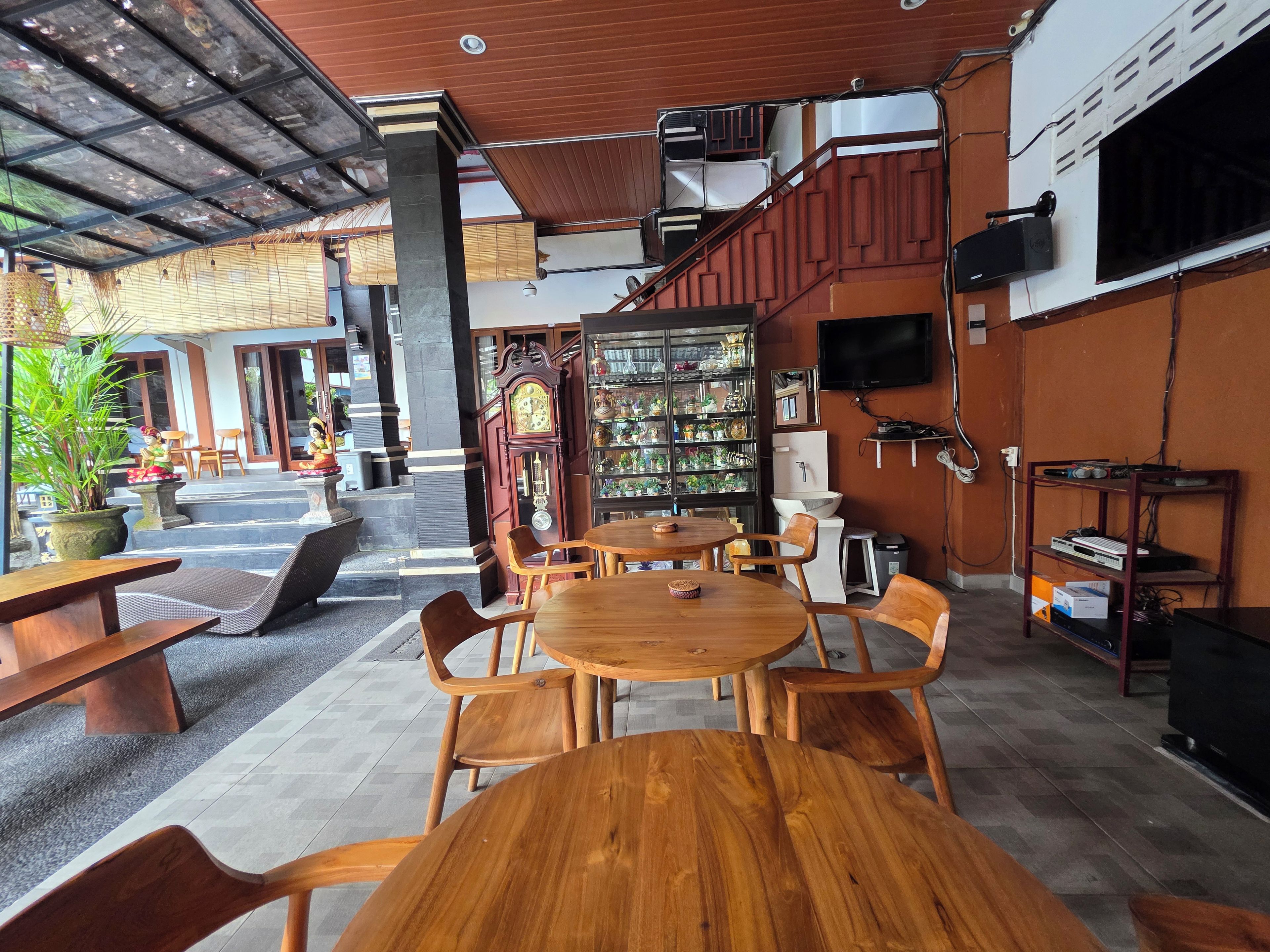 A restaurant with wooden tables and chairs, a clock, and a shelf with various items.