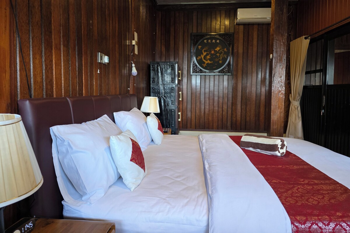 A hotel room with a large bed, a bedside table, a lamp, a wall-mounted air conditioner, and a decorative wall piece.