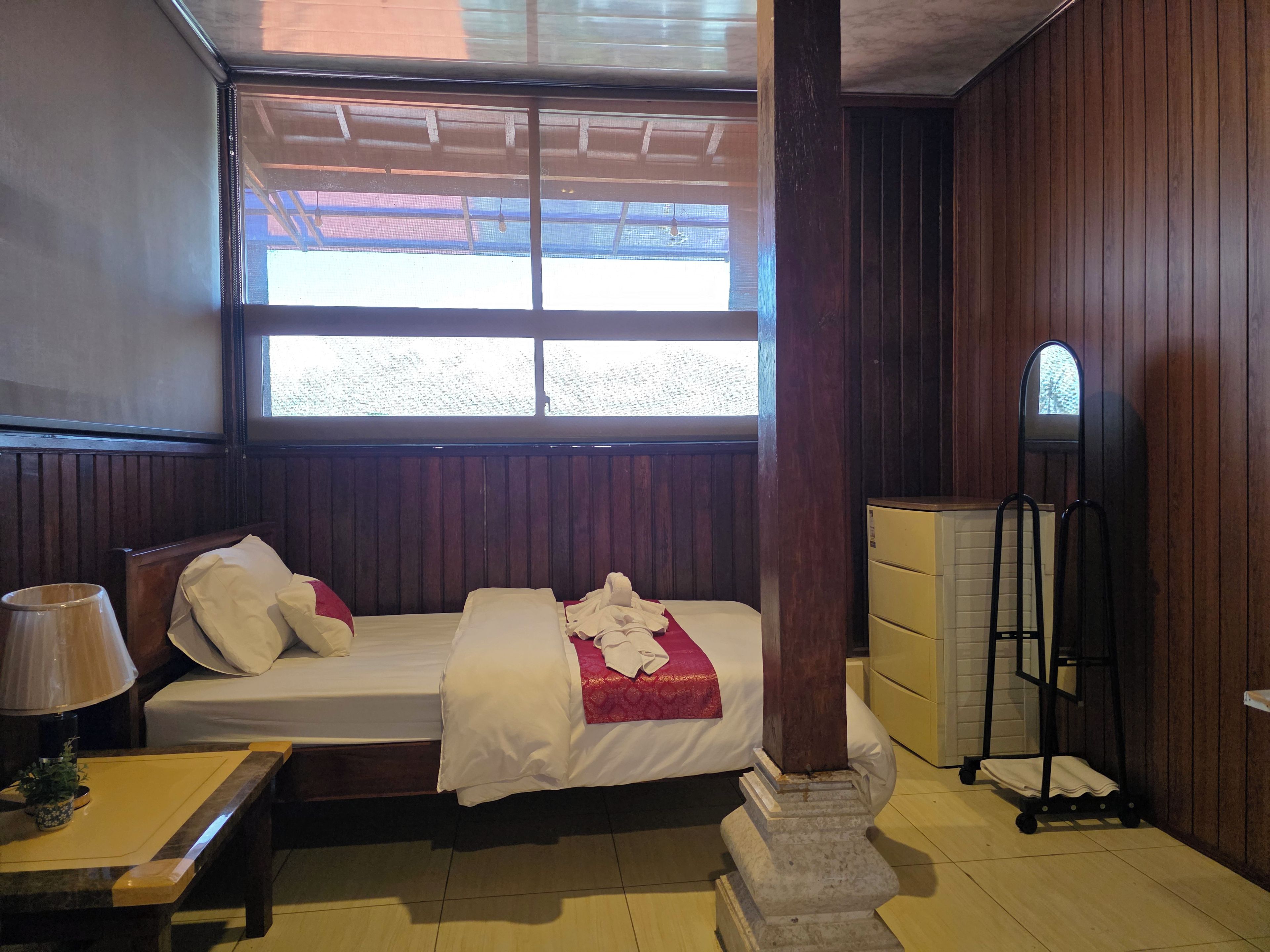 Quarto com cama, mesa de cabeceira, abajur, cômoda e janela.