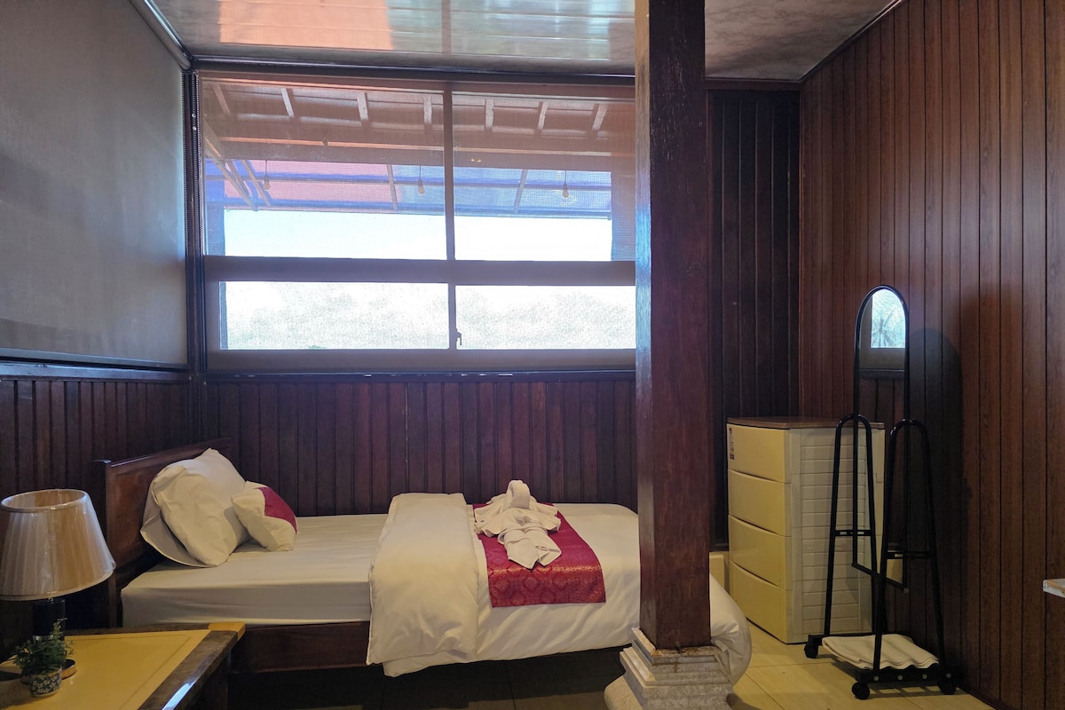 A room with a bed, a nightstand, a lamp, a dresser, and a window.