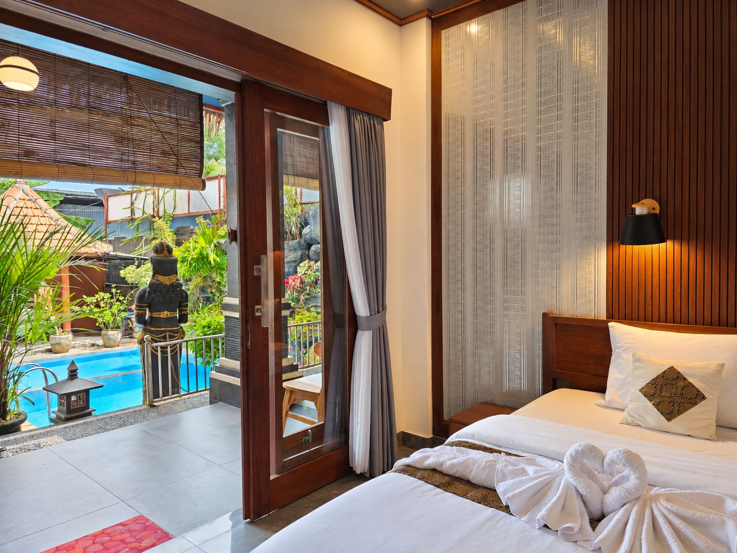 Habitación de hotel con cama, vista a una piscina y balcón con plantas.