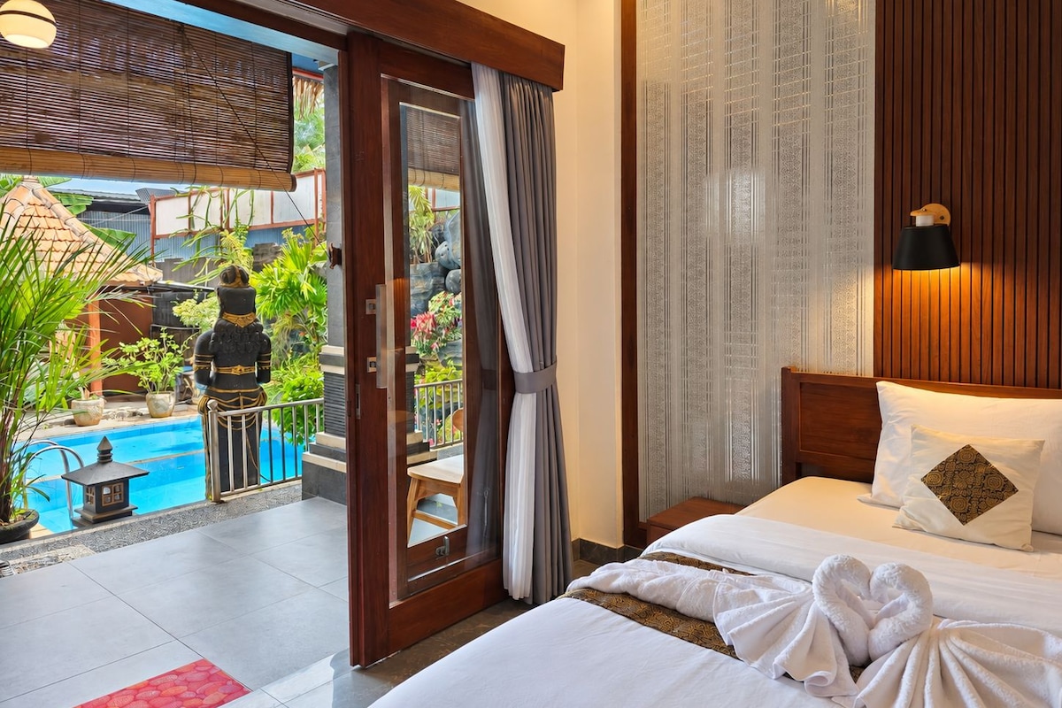 A hotel room with a bed, a view of a swimming pool, and a balcony with plants.