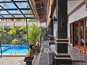 A poolside area with a clear view of the pool, a covered seating area, and a stone wall with plants. - Dahlia Moon Saba Beach (Blahbatuh)