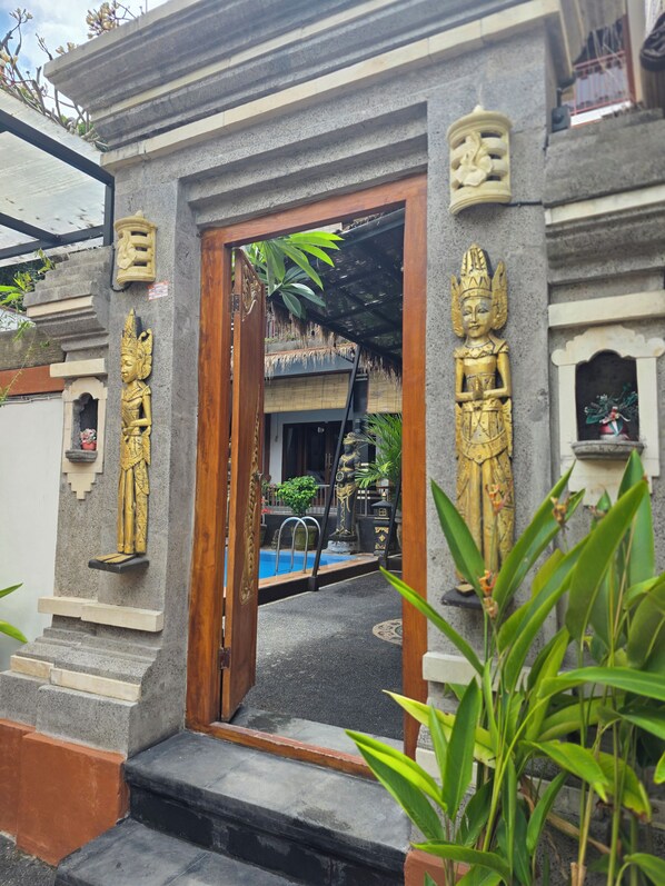 A temple entrance with steps leading up to a wooden door, surrounded by stone carvings and a small pool area.