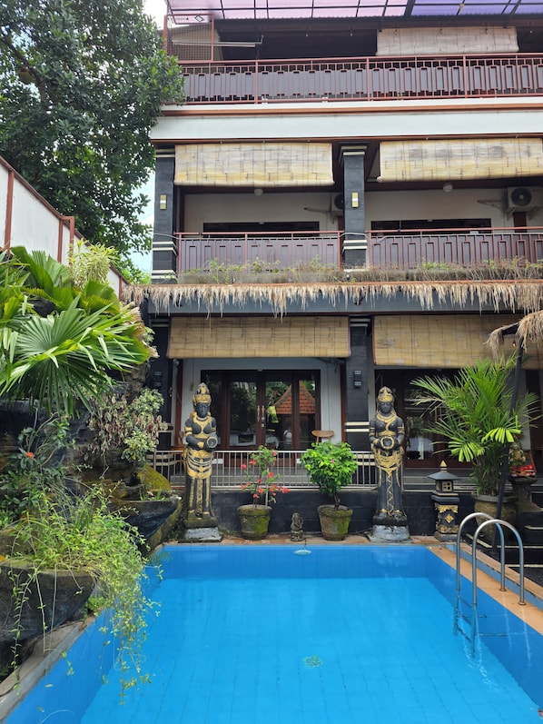 A building with a pool, statues, and tropical plants.