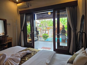 A hotel room with a bed, a seating area with a chair, and a view of an outdoor area with a statue and plants.