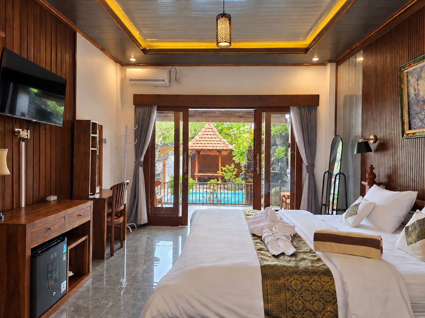 A hotel room with a bed, a desk, a television, and a view of a swimming pool.