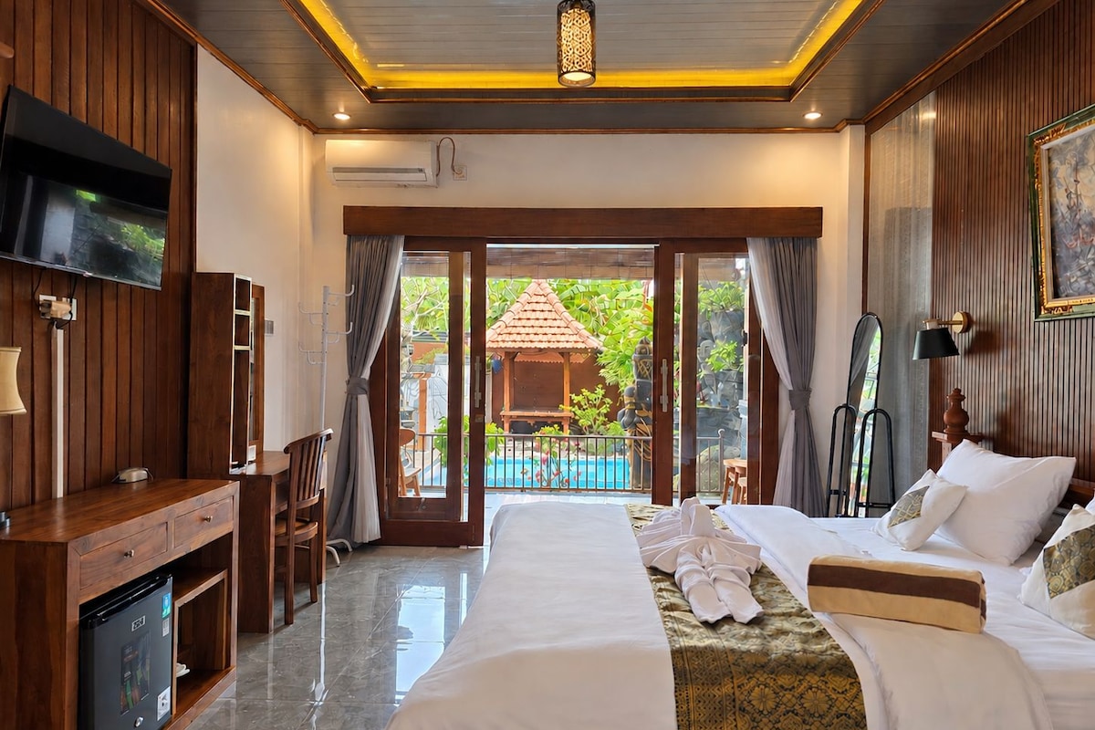 A hotel room with a bed, a desk, a television, and a view of a swimming pool.