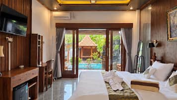 A hotel room with a bed, a desk, a television, and a view of a swimming pool.