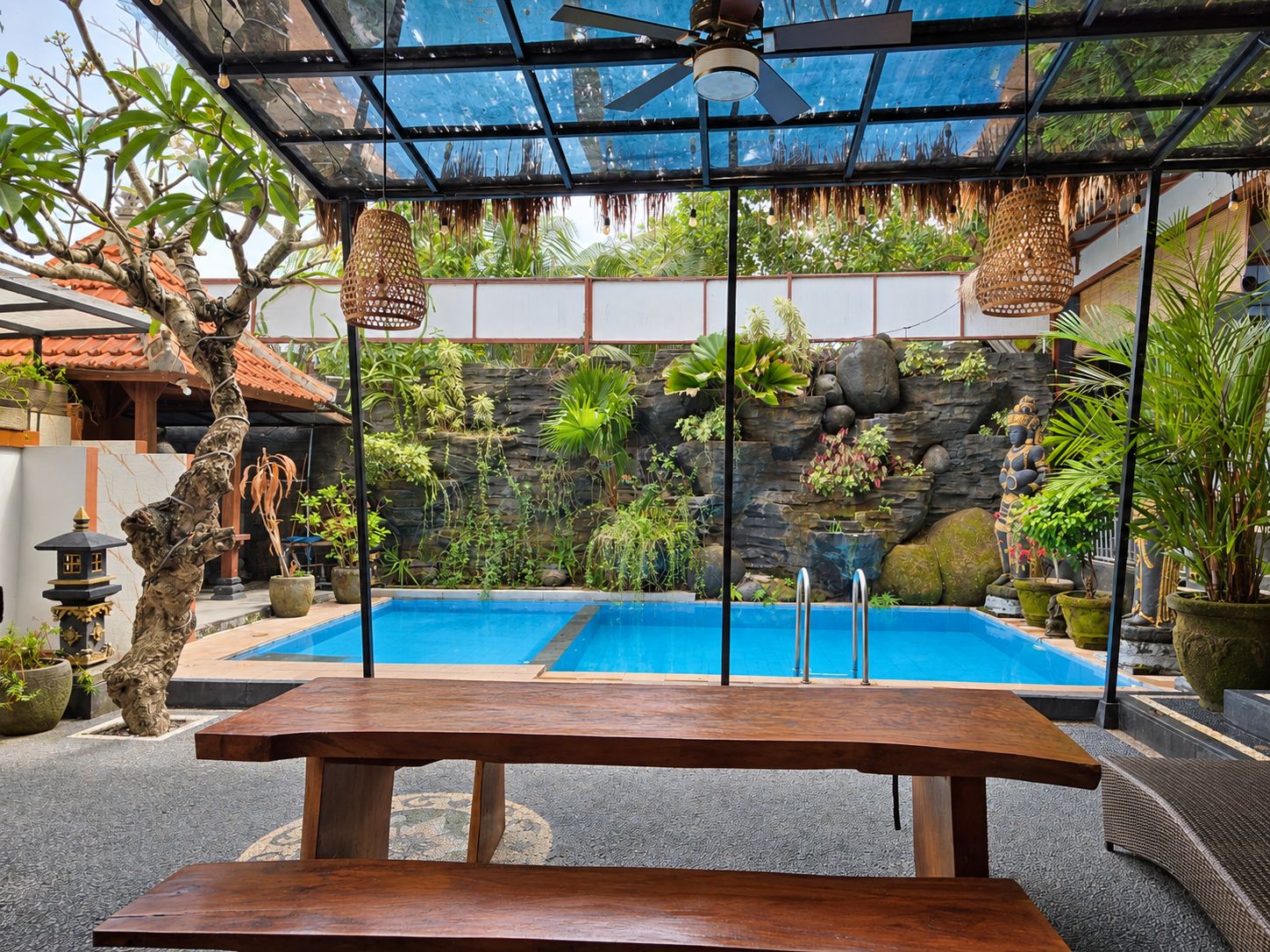 A pool area with a wooden bench, a ceiling fan, and various plants.
