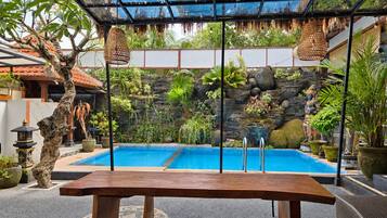 A pool area with a wooden bench, a ceiling fan, and various plants.