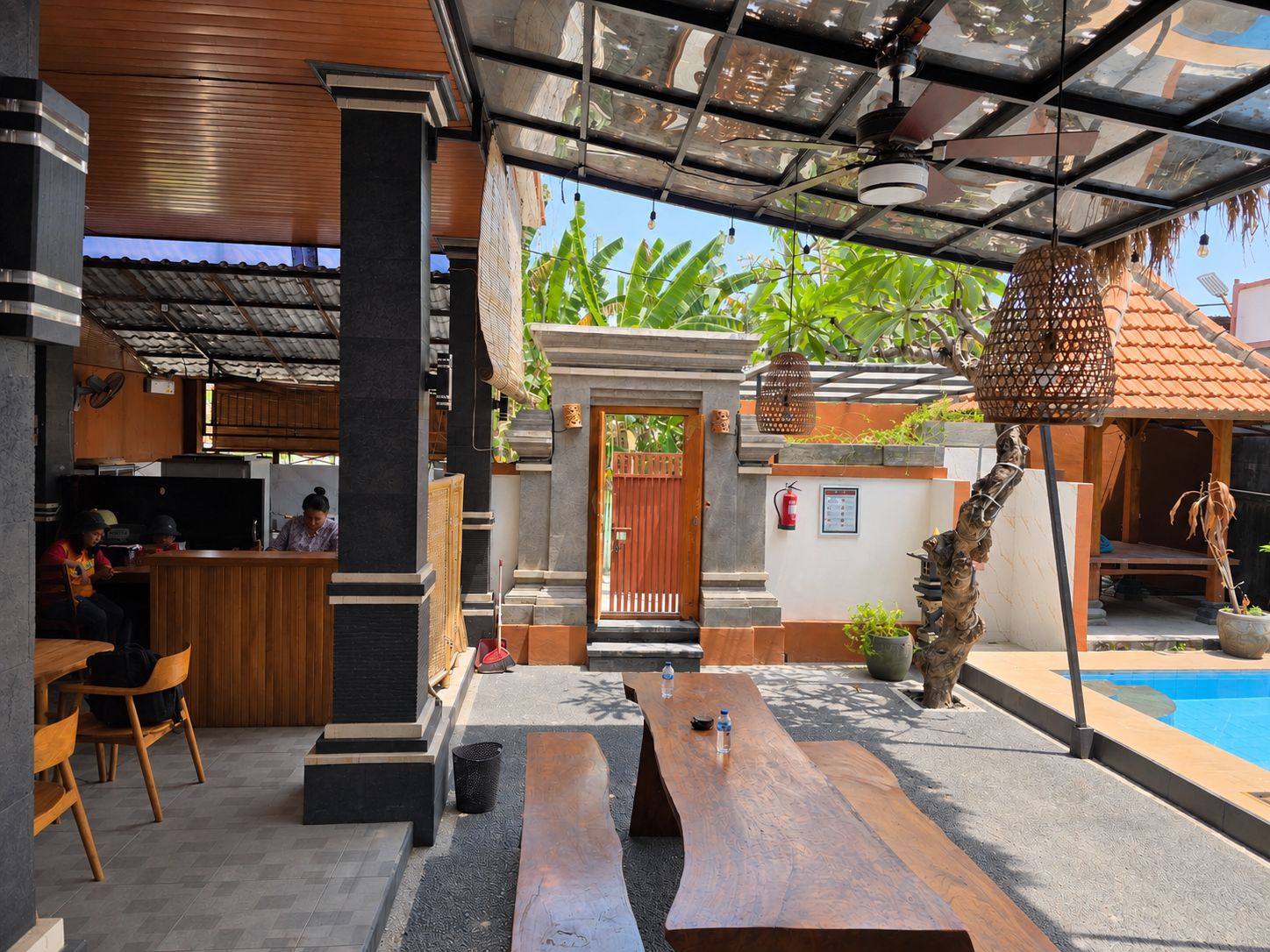 An outdoor seating area with wooden benches and tables, a pool, and a covered entrance with a door.