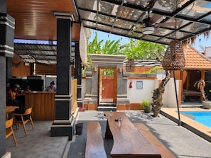 An outdoor seating area with wooden benches and tables, a pool, and a covered entrance with a door.
