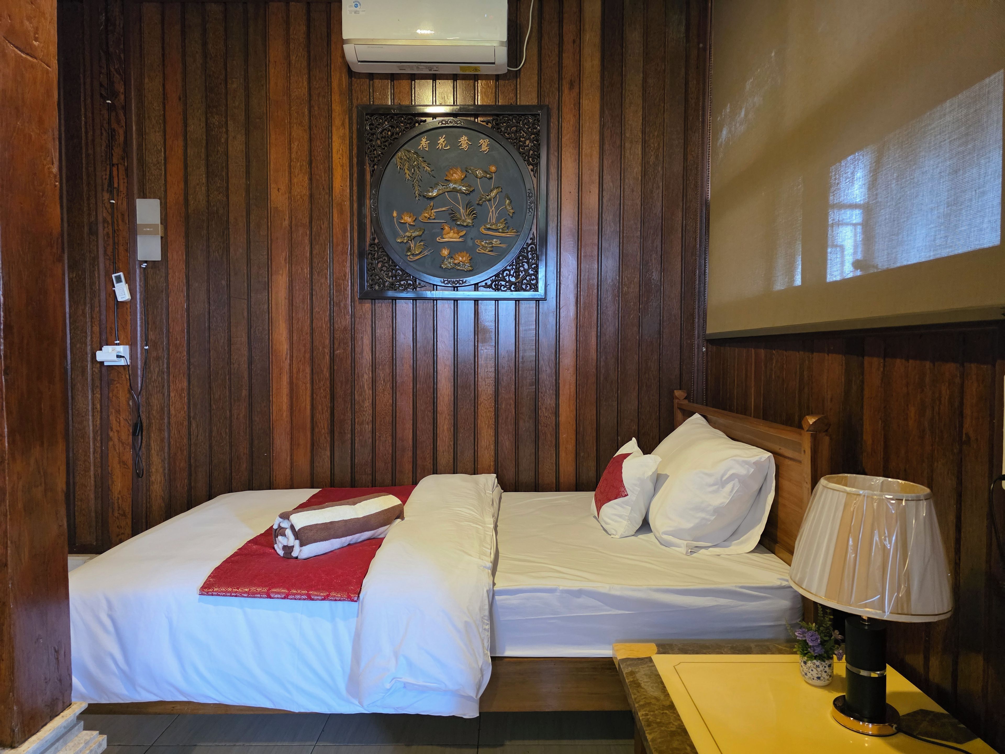 A room with two beds, a wall-mounted air conditioner, a decorative plaque, and a bedside lamp.
