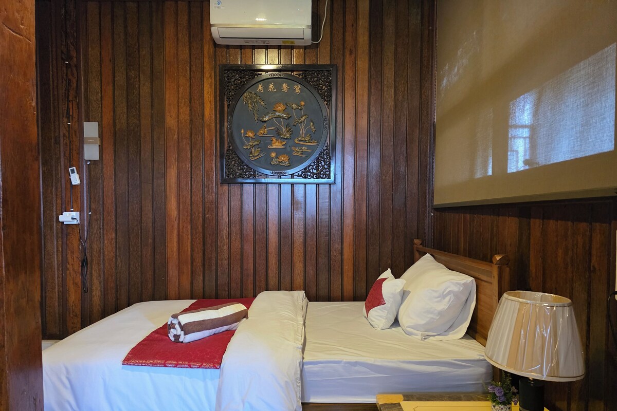 A room with two beds, a wall-mounted air conditioner, a decorative plaque, and a bedside lamp.