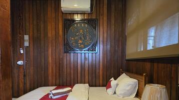 A room with two beds, a wall-mounted air conditioner, a decorative plaque, and a bedside lamp.