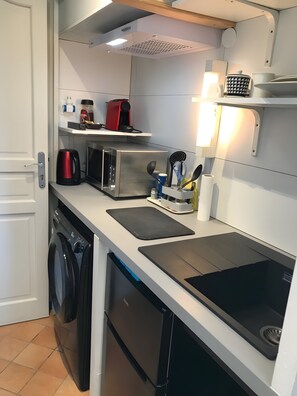 Eine kompakte Küche mit Waschmaschine, Mikrowelle und Kaffeemaschine auf der Arbeitsplatte.