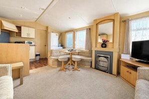 Interior compacto de una caravana con kitchenette, comedor, zona de estar y televisor.