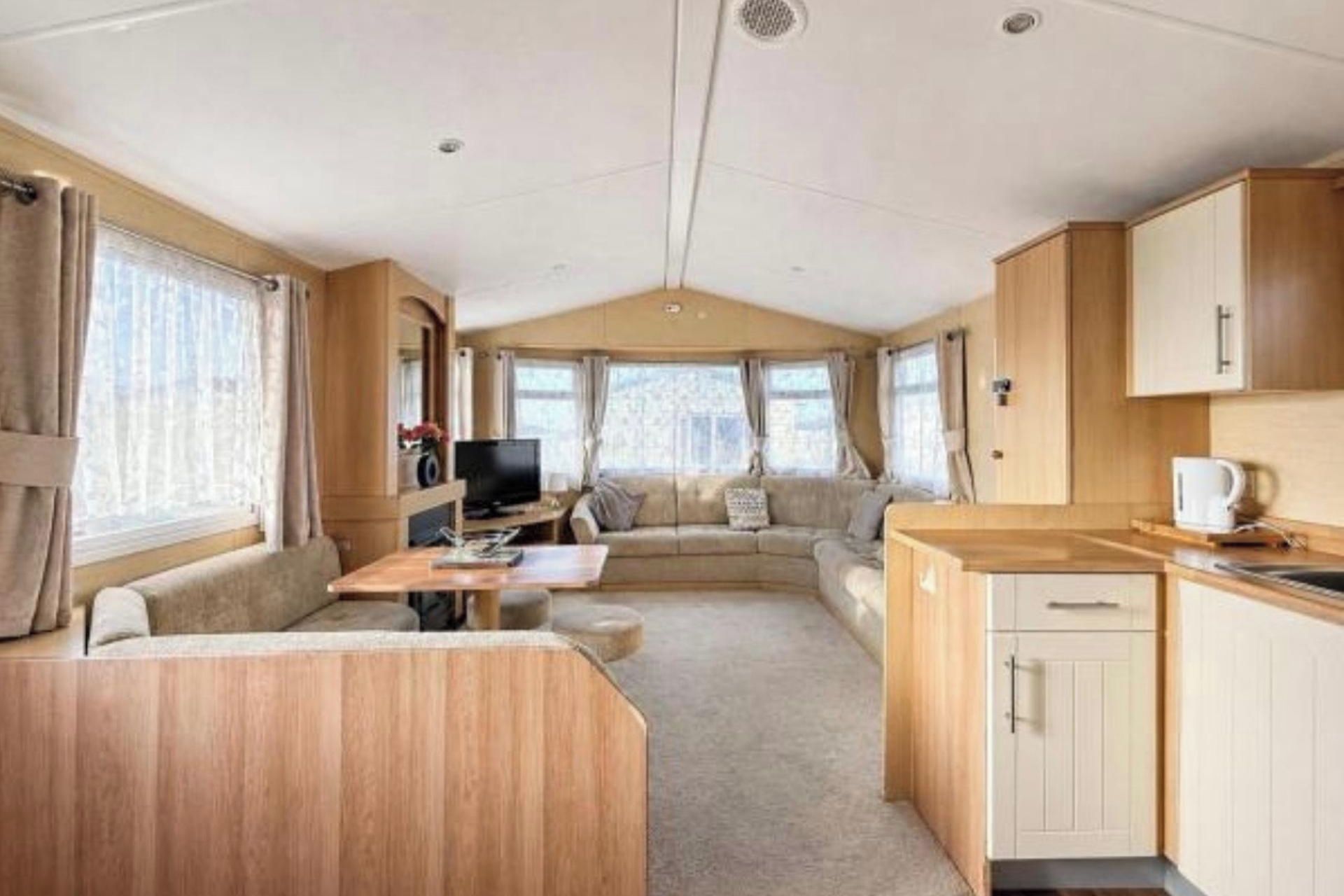 Interior de una caravana con zona de estar, kitchenette y televisor.