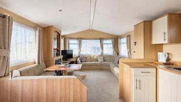 Interior de una caravana con zona de estar, kitchenette y televisor.